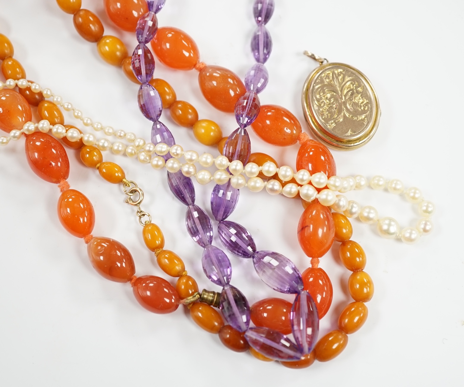 A gold plated oval locket and four assorted single strand necklaces including cultured pearl, amber, agate and amethyst.